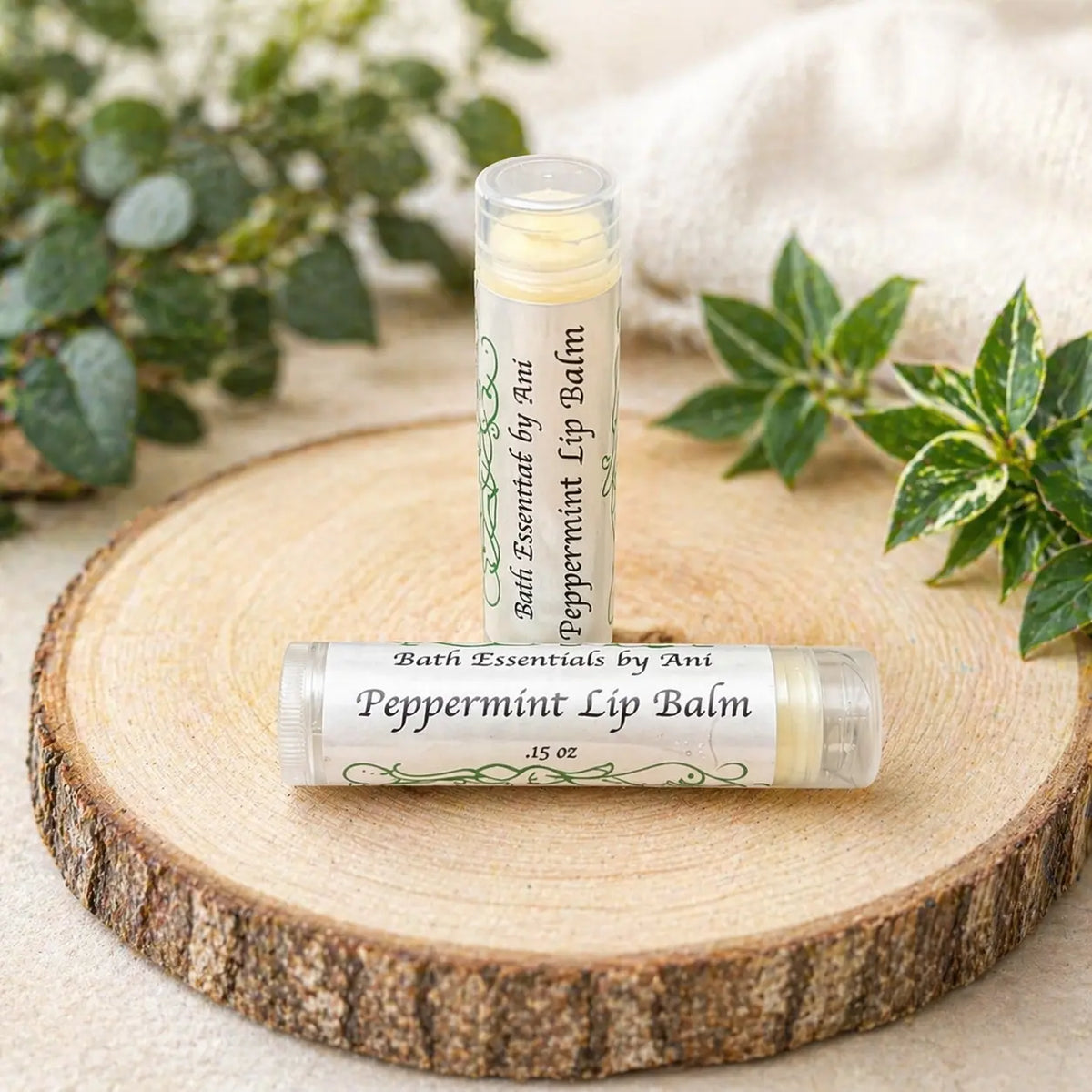 Peppermint lip balm tube on wooden slice with clear lip balm cap and greenery