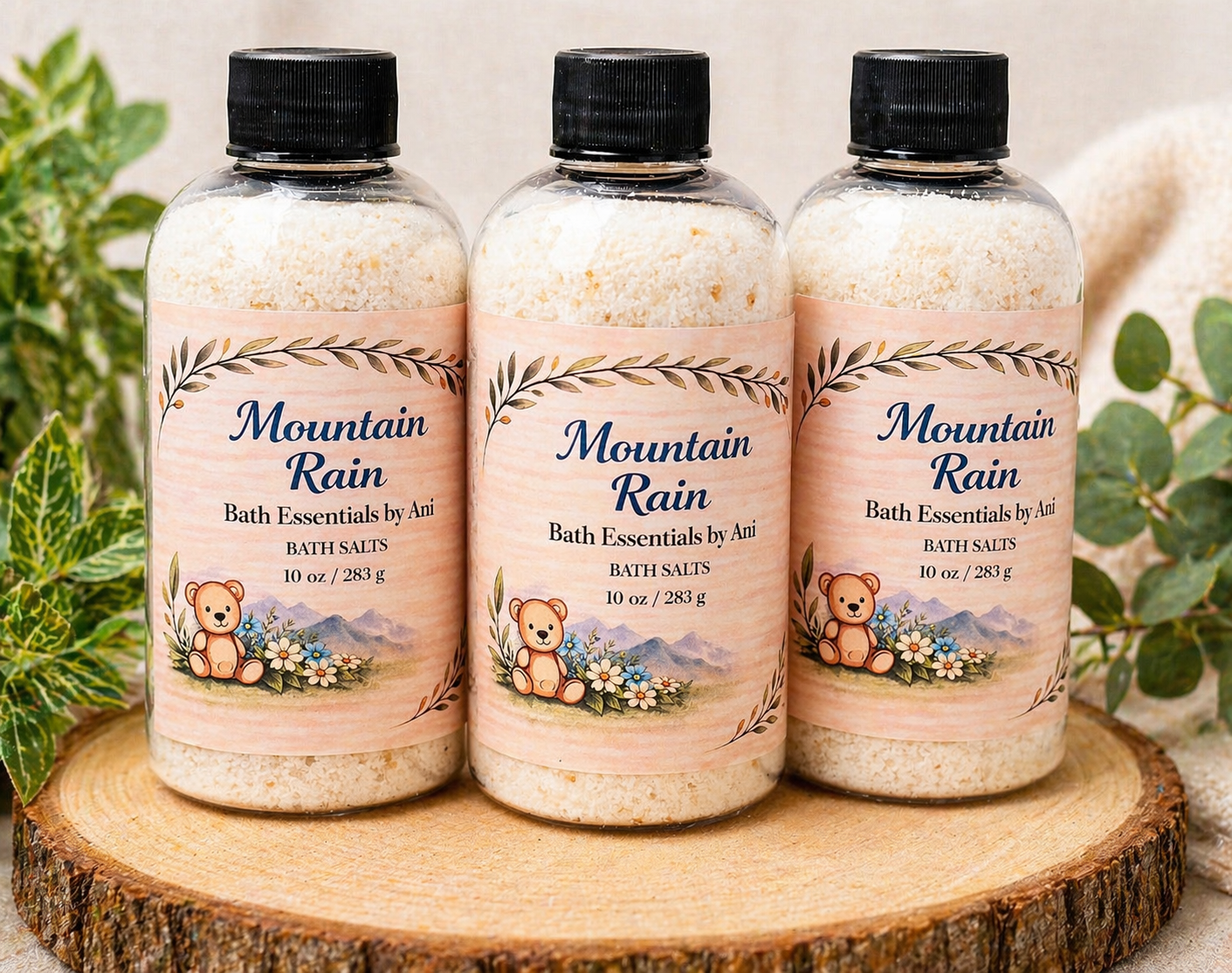 Three Mountain Rain bath salts bottles on wooden slice with greenery in the background