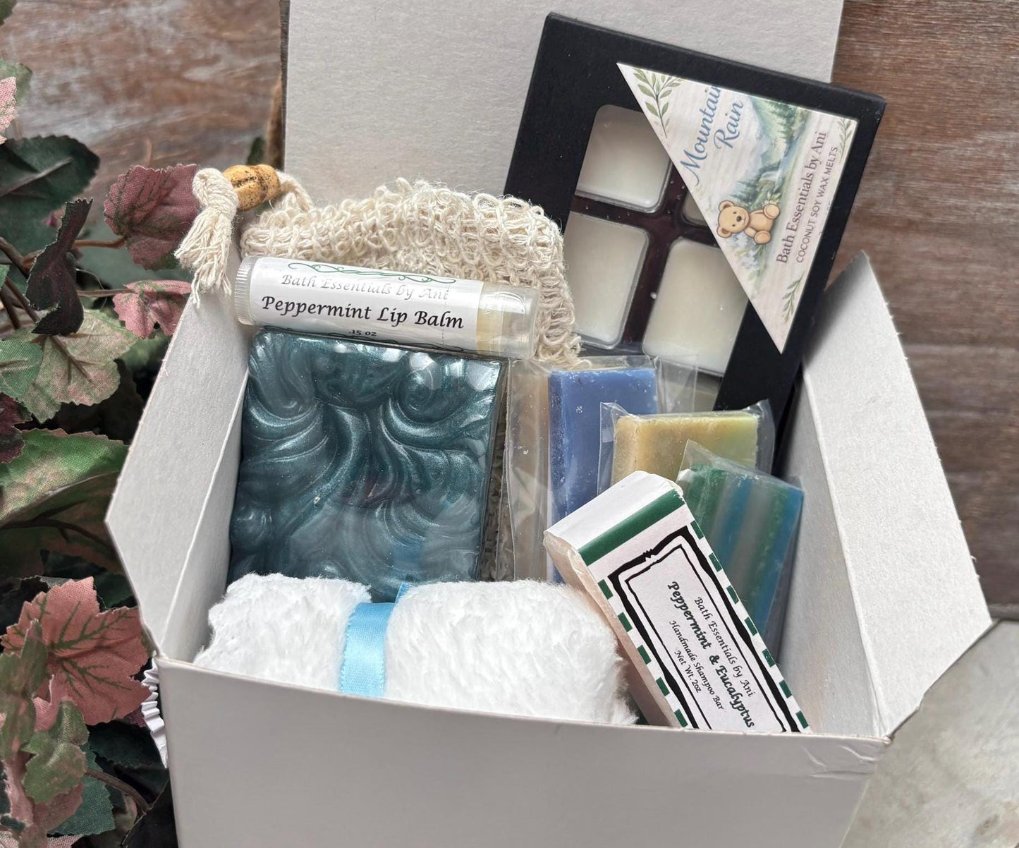 Bath gift box with teal soap bars, lip balm tubes, white bath bomb, and knit pouch
