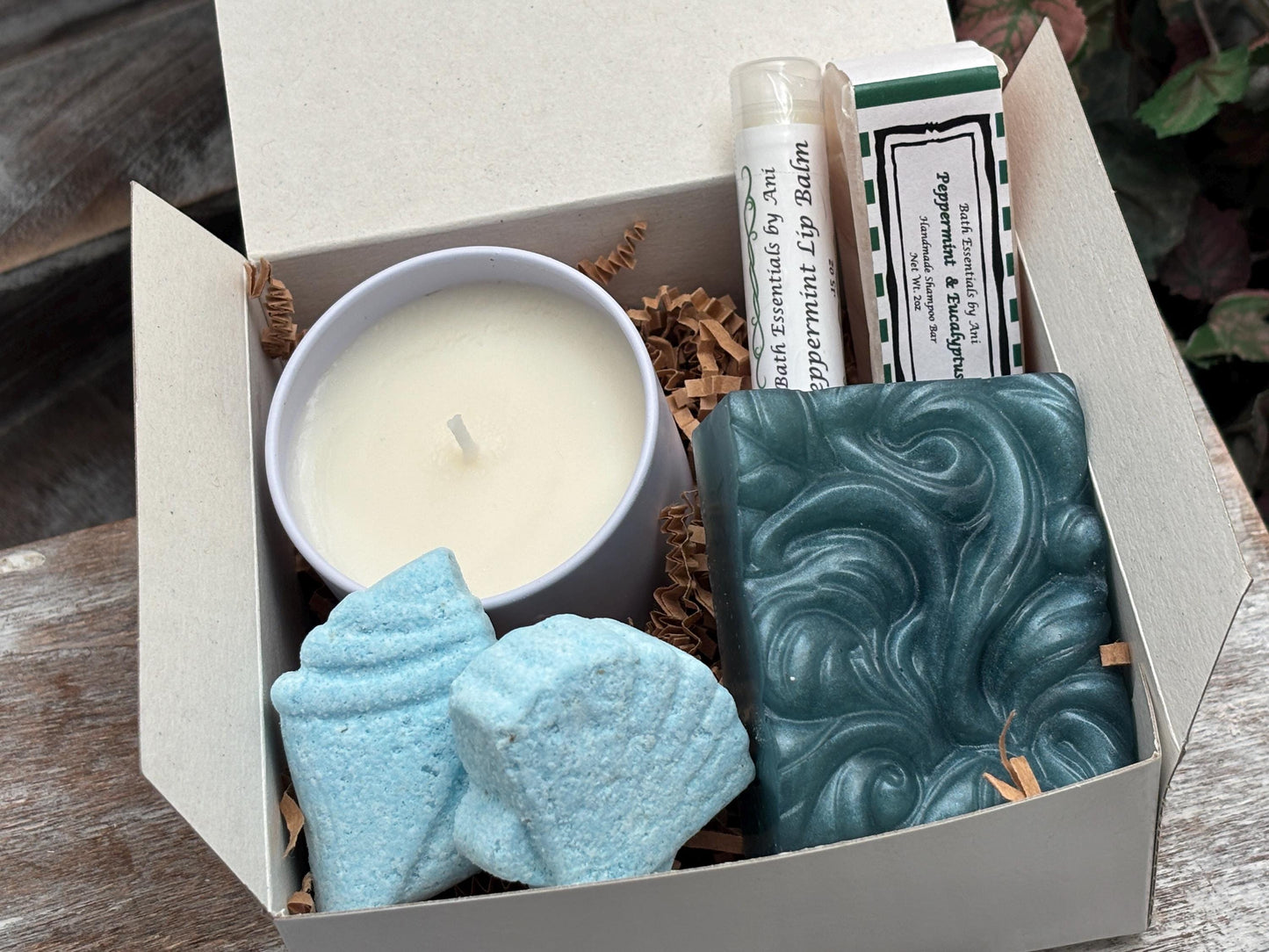 Open gift box with white candle, teal swirled soap bar, and blue bath sponge pieces