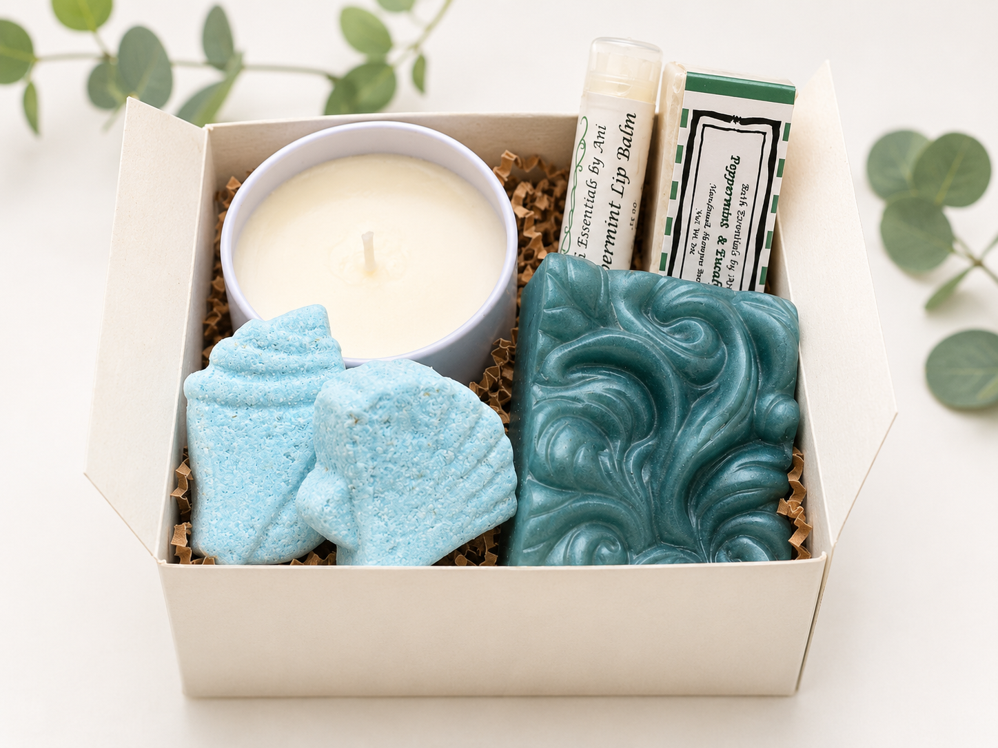 Gift box with white candle, teal swirled soap bar, and blue bath sponge pieces