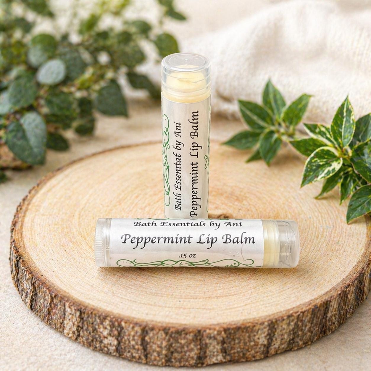 Peppermint lip balm tube and clear wrapper on a round wood slice with bath essentials.