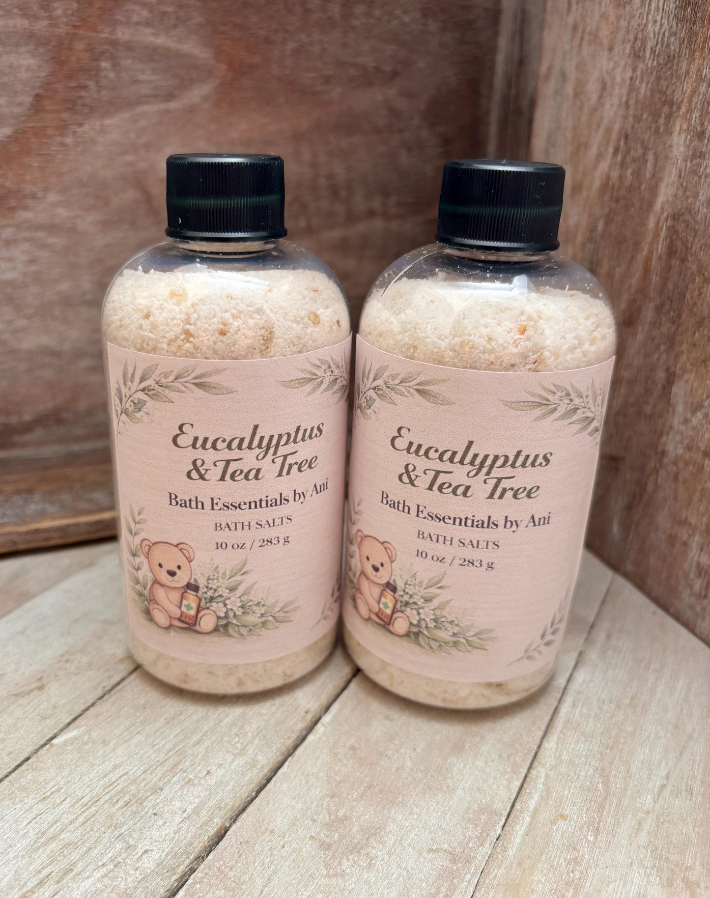 Two eucalyptus tea tree bath essentials bottles with black caps on a wooden surface