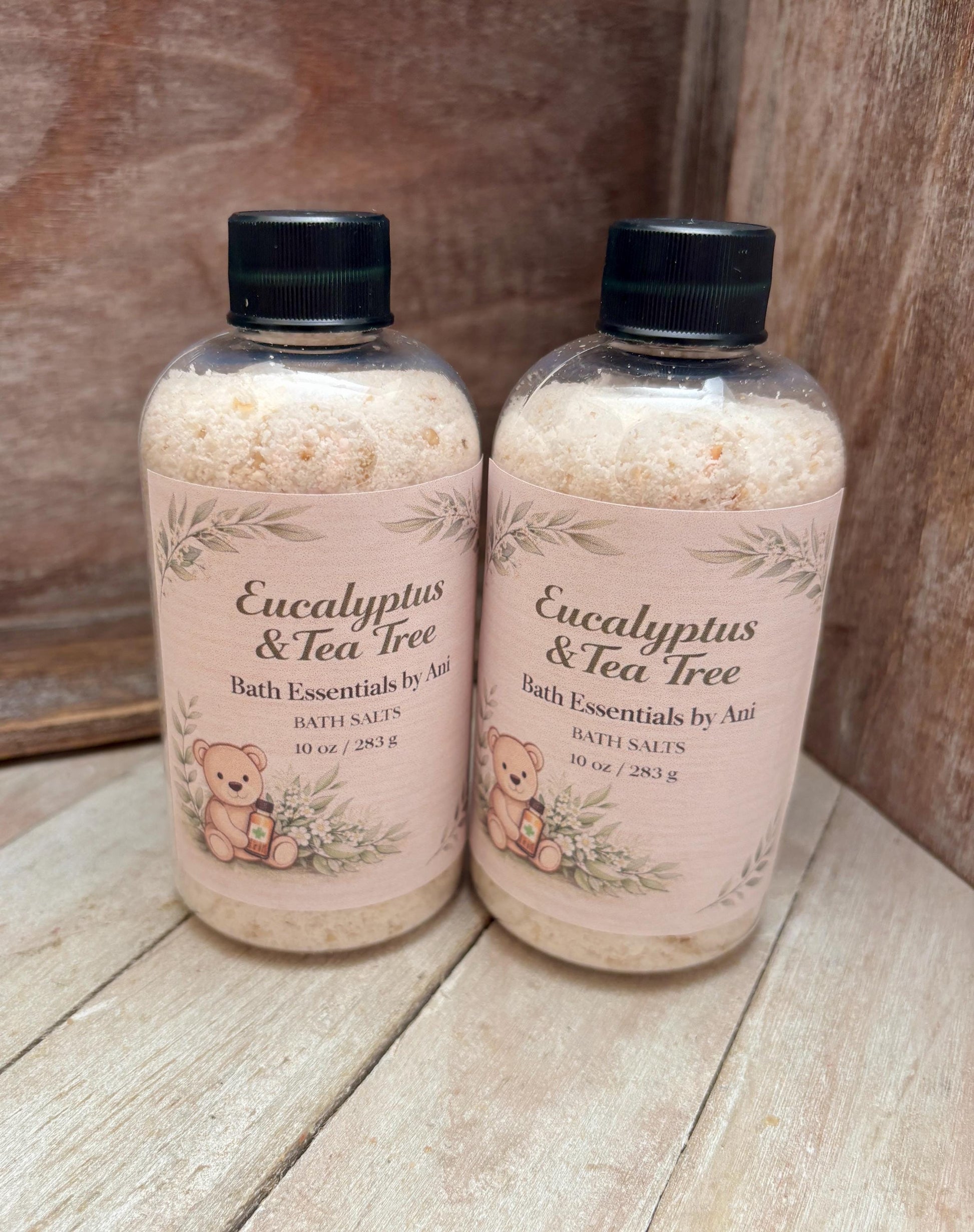 Two eucalyptus tea tree bath essentials bottles with black caps on a wooden surface