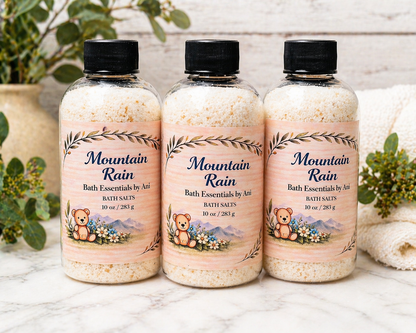 Three bath essentials bottles with black caps and Mountain Rain label, speckled bath salts
