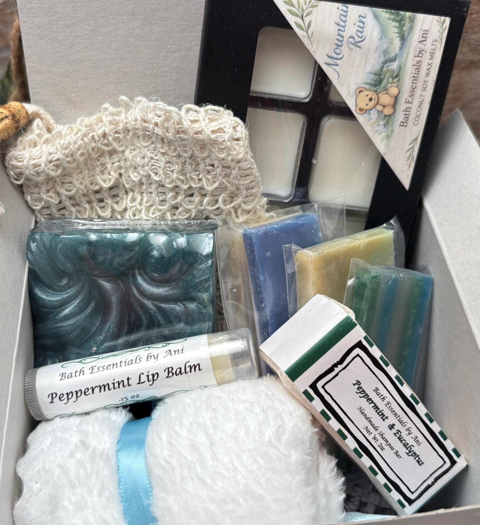 Bath gift box with knit scrub pouch, teal soap bars, wrapped bath products, and lip balm