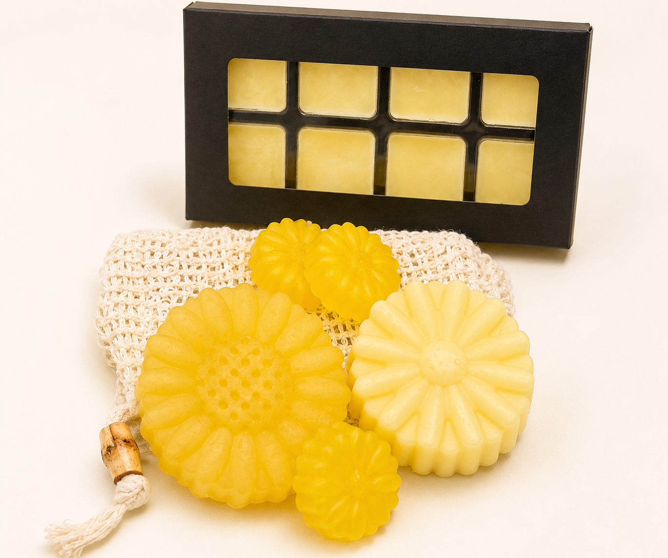 Yellow flower-shaped soaps on mesh pouch with black wax melt tray gift box behind.