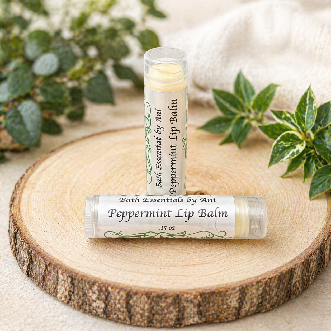 Peppermint lip balm tube on a wood slice with a candle and green leaves