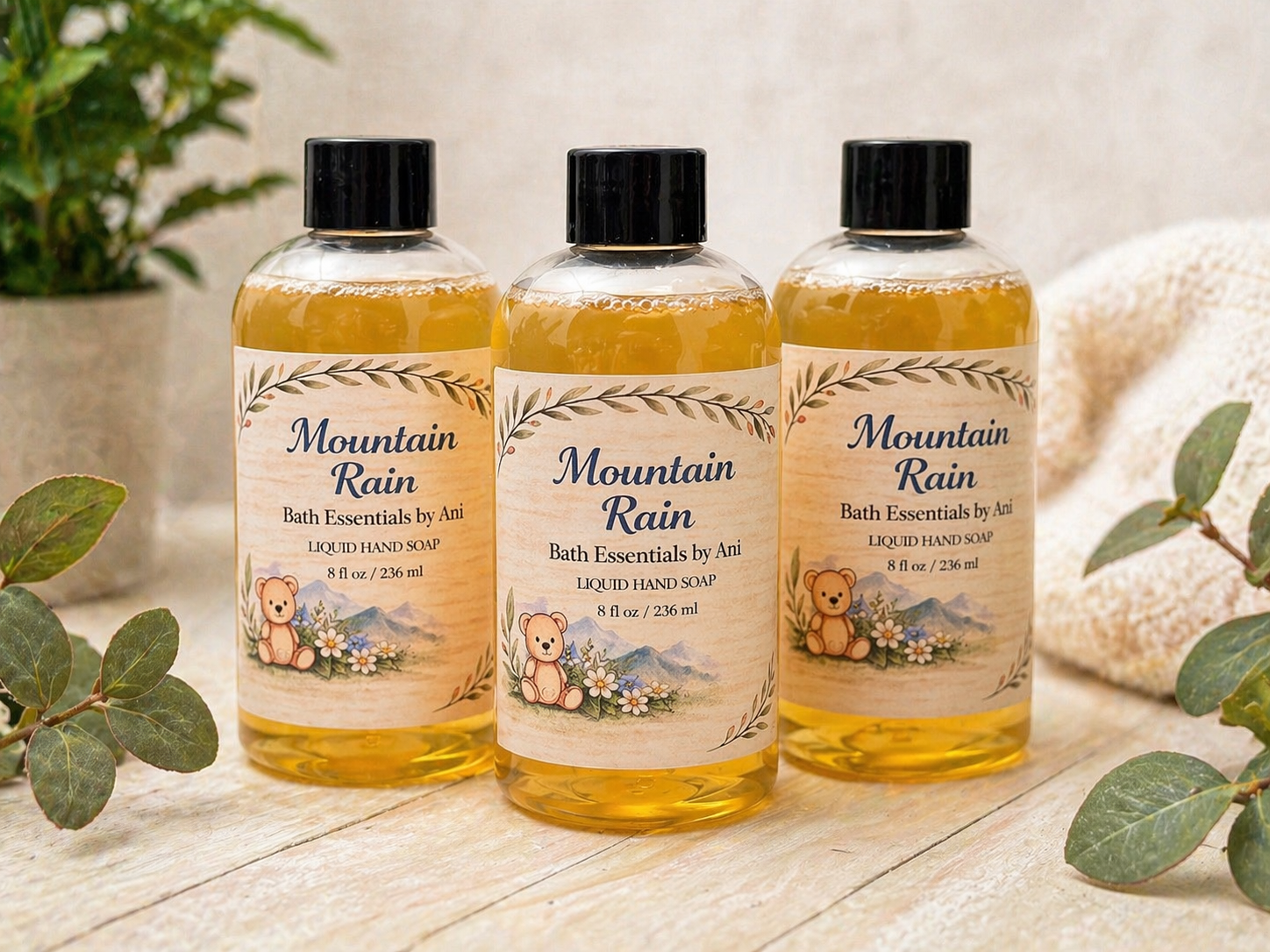 Three bath essentials bottles with black caps and Mountain Rain label, amber liquid