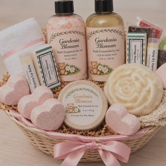 Deluxe Gardenia spa gift basket with handmade soaps, bath salts, scented candle, heart bath bombs and self-care essentials in a wicker basket with pink ribbon.