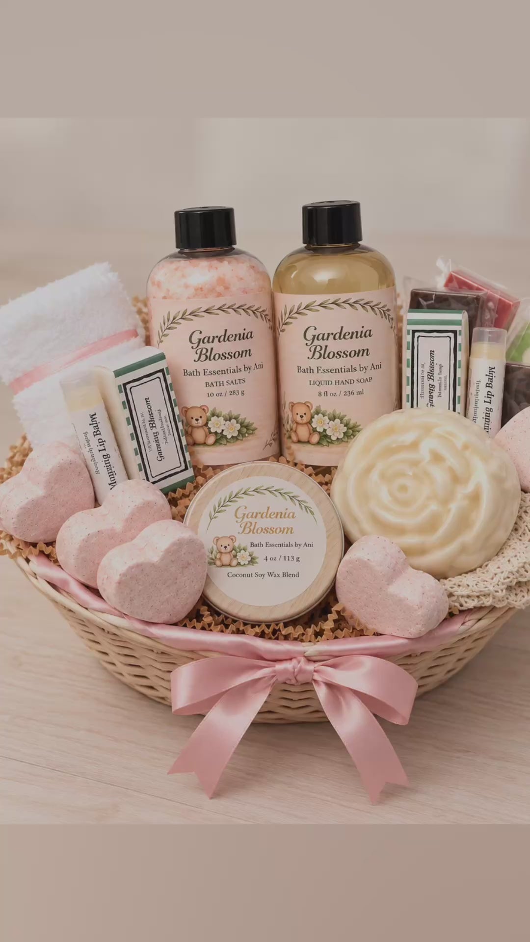 Deluxe Gardenia spa gift basket with handmade soaps, bath salts, scented candle, heart bath bombs and self-care essentials in a wicker basket with pink ribbon.